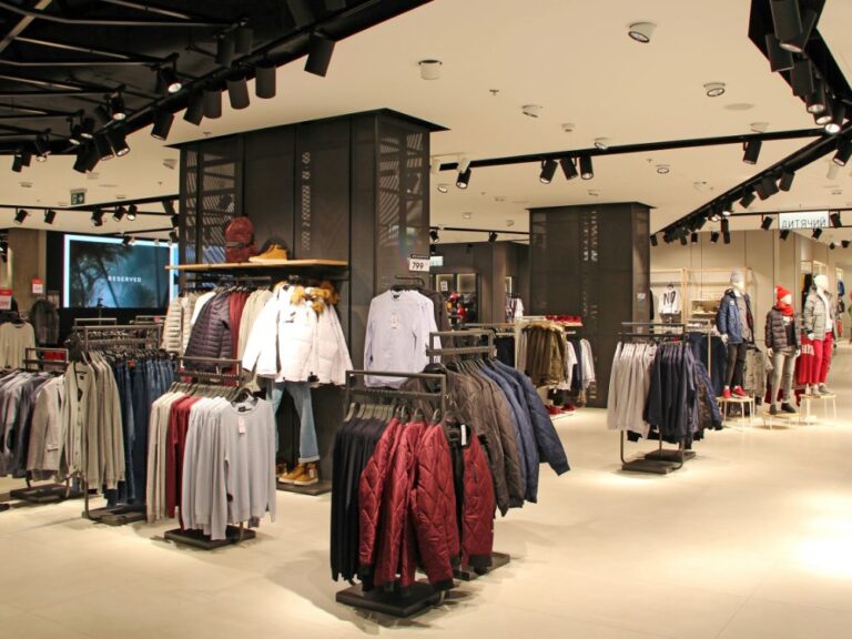 Interior de loja de roupas com araras organizadas e peças expostas para venda, ilustrando como investir em loja de roupas e estruturar um ponto comercial de moda.