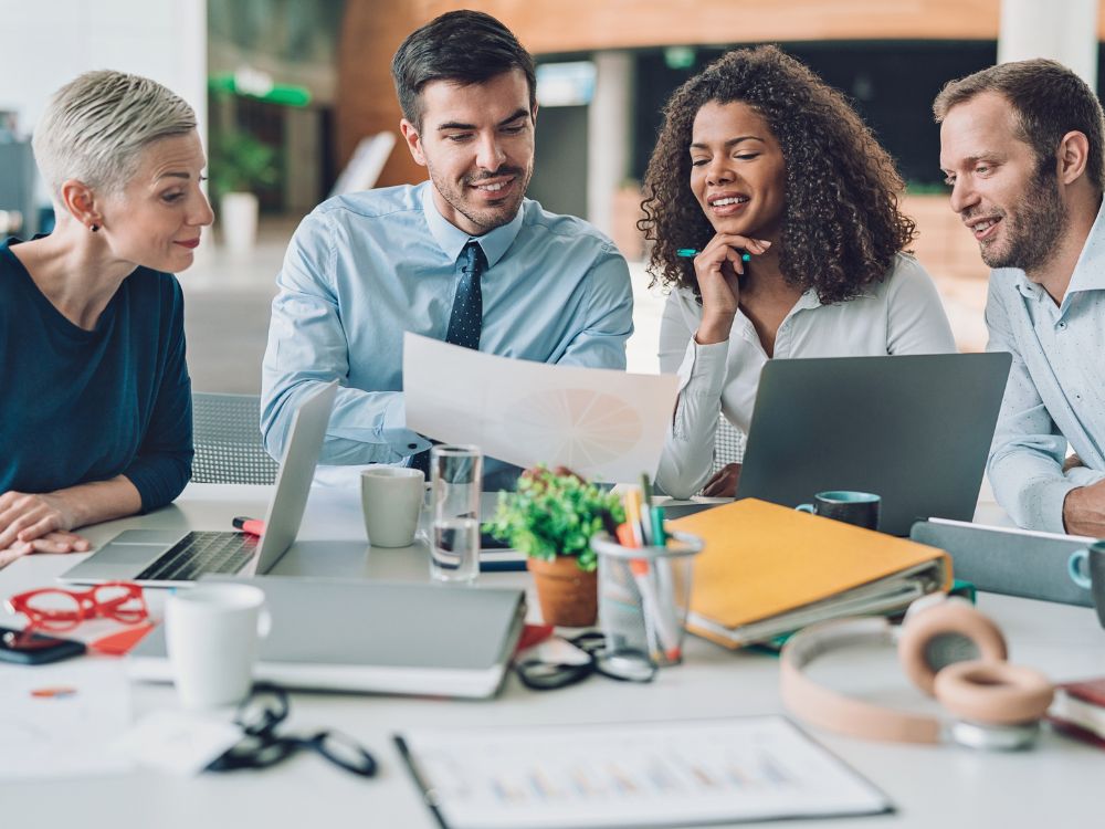 Profissionais reunidos em ambiente corporativo analisando documentos e estratégias de marketing, ilustrando ações de reconhecimento de marca e planejamento de ativação de marca em eventos.